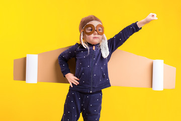 Freedom, girl playing to be airplane pilot, funny little girl with aviator cap and glasses, carries wings made of brown cardboard as an airplane