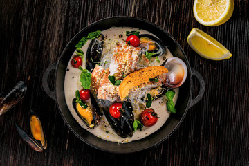 Delicious Asian meal made of sea bass fish, mussels, crab meat and other seafood with tomato and rice noodles on a rustic wooden table. Top view.