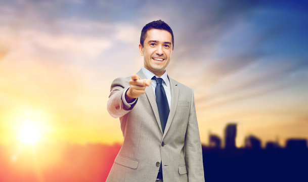 smiling businessman pointing at you over city