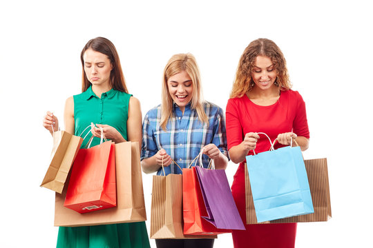 Portrait of three young girlfriends holding bunches of multi-colored shopping bags