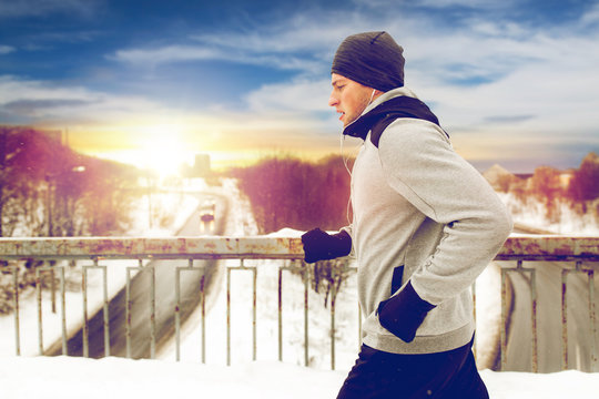 man in earphones running along winter bridge