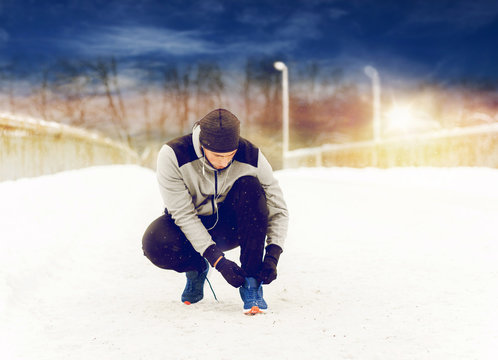man with earphones tying sports shoe in winter