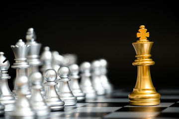 Gold king in chess game face with the another silver team on black background (Concept for company...