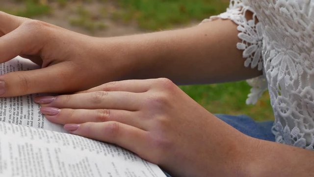4k. Woman Readibg  Bible in park.Body. Slider shot, hands close up