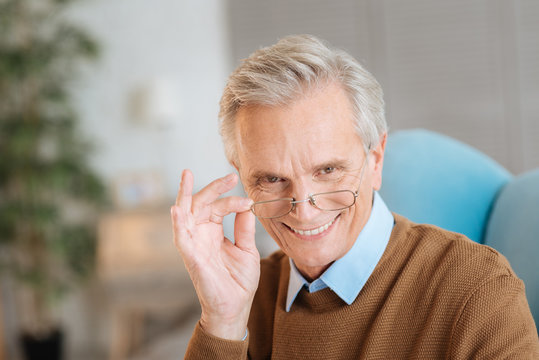 Positivity is the key to success. Portrait of a friendly looking retired man taking off his glasses and smiling cheerfully while looking into the camera with his eyes full of happiness.