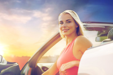 happy woman in convertible car over evening sky