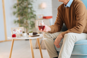 Love never dies. Scaled up look on an old gentleman sitting in a chair and holding a glass of red wine while celebrating anniversary with his wife.