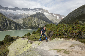 Fototapeta na wymiar Hiker hikes through a wild high alpine landscape with a lake and glacier in the background, Switzerland