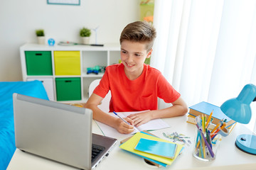 student boy with laptop writing to notebook
