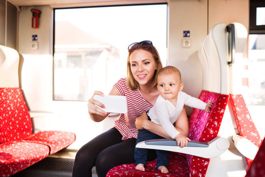Young mother with smartphone travelling with baby by train.