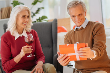 Is this for me. Selective focus on a radiant senior gentleman cannot keep his emotions inside and smiling after receiving a surprise present from his loving wife.