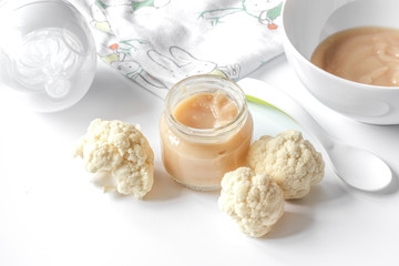 baby mashed with spoon in glass jar on white background