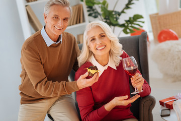 So many years together. Extremely happy retired couple grinning broadly while sitting next to each other and celebrating their wedding anniversary in a tight family circle.