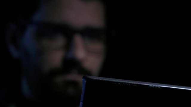 Hacker working on laptop, focus pull, wearing glasses
