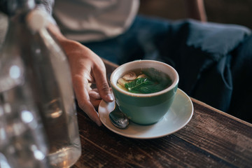 Soft focus shot of hand holding cup with fresh mint and ginger tea or infusion, served in cafe or coffee shop on cold winter morning, concept cosy, hot beverage and flu home medicine