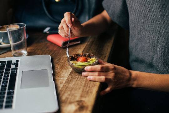 Soft focus shot of woman at coworking space or cafe with internet connection, work on laptop and enjoy small dessert made from chia seeds pudding and fruits