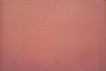 The red background. Painted metal surface. The surface of the train as a background element. Metal painted in red. Iron plates fastened by rivets between
