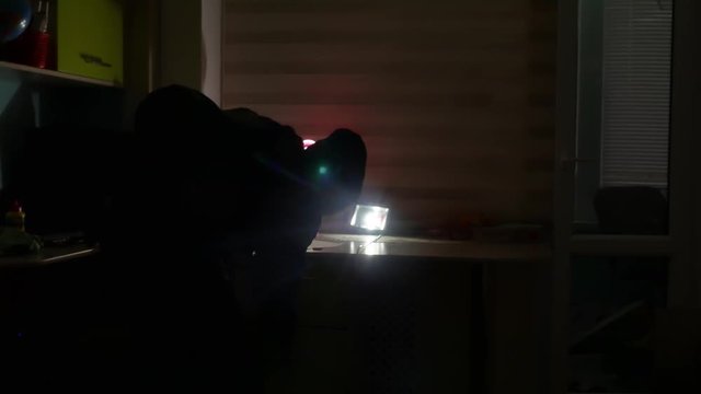 thief in a house silhouette at night steals a indoor laptop and things