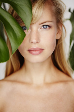 Beautiful blond woman looking through leaf in studio
