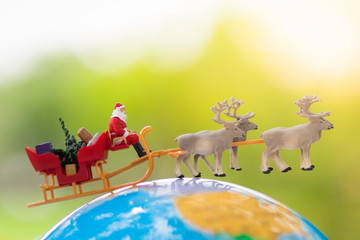 Miniature Santa Claus drive a wagon with a reindeer during the snowfall on world map. Using as concept in Christmas day.