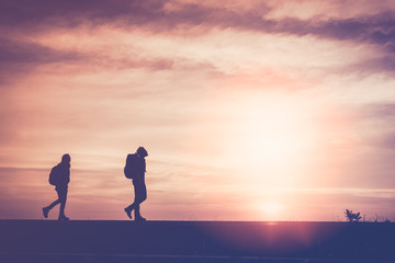Silhouette of couple travelers are walking on the Beach road at sunset. The concept of lovers and tourist traveler
