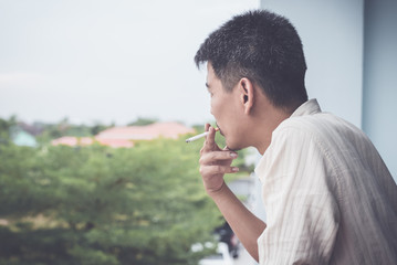 Asian man smoking on the balcony bedroom.