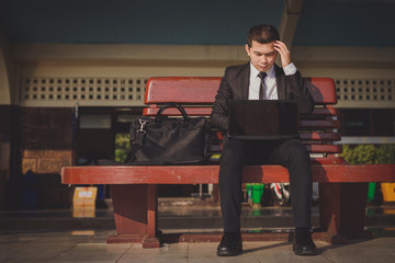 Young asian businessman feel stressed/worry/headache/disappoint during working  while sit at train station,working on computer laptop online ,vintage photo and film style.