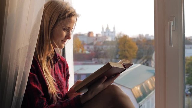 Beautiful young woman reads old book near the window