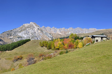 Naklejka premium peak mountain and cottage on a hill in autumn under blue sky 