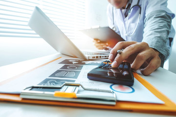 Fototapeta premium Healthcare costs and fees concept.Hand of smart doctor used a calculator and smartphone for medical costs at modern hospital in sun light