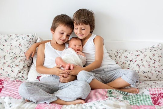 Two children, toddler and his big brother, hugging and kissing their newborn baby brother at home, few days after delivery