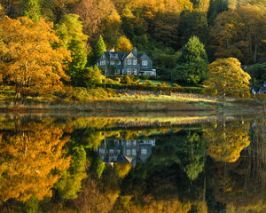 Rural country house reflecting in a calm lake with stunning Autumn colours. Taken at Rydal Water in the English Lake District.