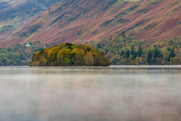 A small island with Autumnal foliage at Derwentwater with beautiful rising lake mist.