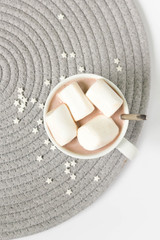 A cup of hot cocoa with marshmallows on grey and white background, top view.