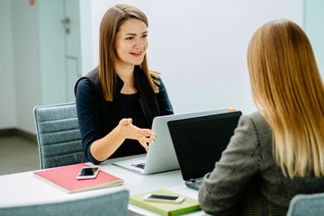 Two friendly female co-workers having discussion or interview while sitting face to face with...