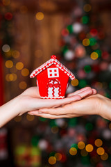 Human hands holding decorative red house against blurred background. Christmas and home comfort concept.