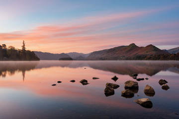 Beautiful pink sunrise reflected in a calm misty lake with rocks in foreground. Taken at...