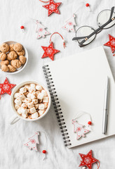 Hot chocolate with marshmallows and cinnamon, clean blank notepad, christmas decorations on a light background. Christmas inspiration planning concept