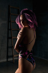 young sexy girl with pink curly hair in a colored swimsuit on a black background, Water studio photo