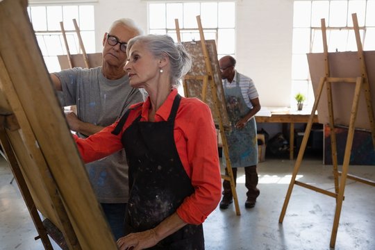 Senior man looking at woman painting on easel