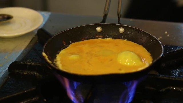 Preparing scrambled eggs in black frying pan on cooker. Real time full hd video footage.
