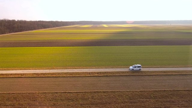 Aerial view of car driving on horizontal line between farm fields 4K