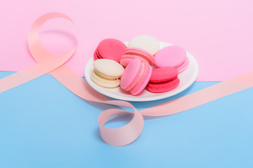 Homemade Colorful macaroons or macaron on White plate with pink ribbon on pink and blue pastel background