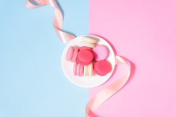 Homemade Colorful macaroons or macaron on White plate with pink ribbon on pink and blue pastel...