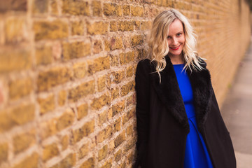 The young elegant beautiful woman standing outdoor near brick wall