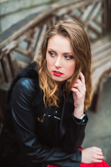 Portrait of young beautiful thinking woman who sitting on wooden bench outdoors