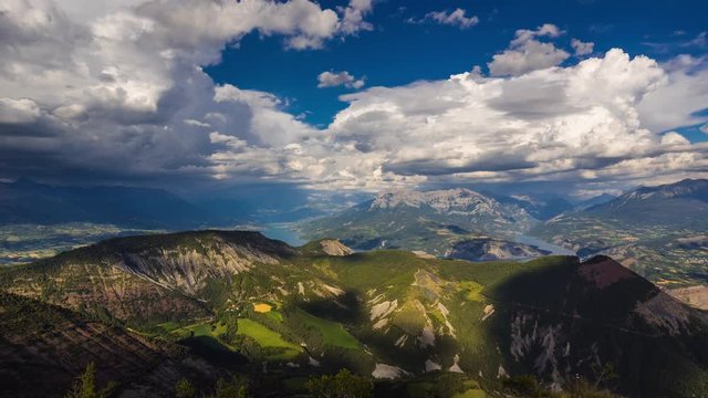 Aerial view of Serre-Poncon Lake with passing clouds in Summer. The view includes Savines-le-Lac village and the Grand Morgon peak. Hautes-Alpes timelapse, Durance Valley, Southern French Alps, France