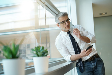 Businessman talking on phone in office, standing by window