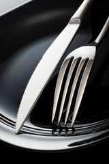 Empty plate with spoon, knife and fork on a black background