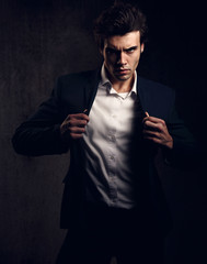 Charismatic sexy male model posing and holding the fashion suit and white style shirt looking energetic on dark shadow background. Closeup toned portrait